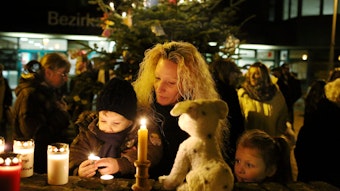 Ein Kind entzündet eine weitere Kerze und stellt sie mit seiner Mutter neben ein Stofftier zum Gedenken an die ermordete Lea Sofie