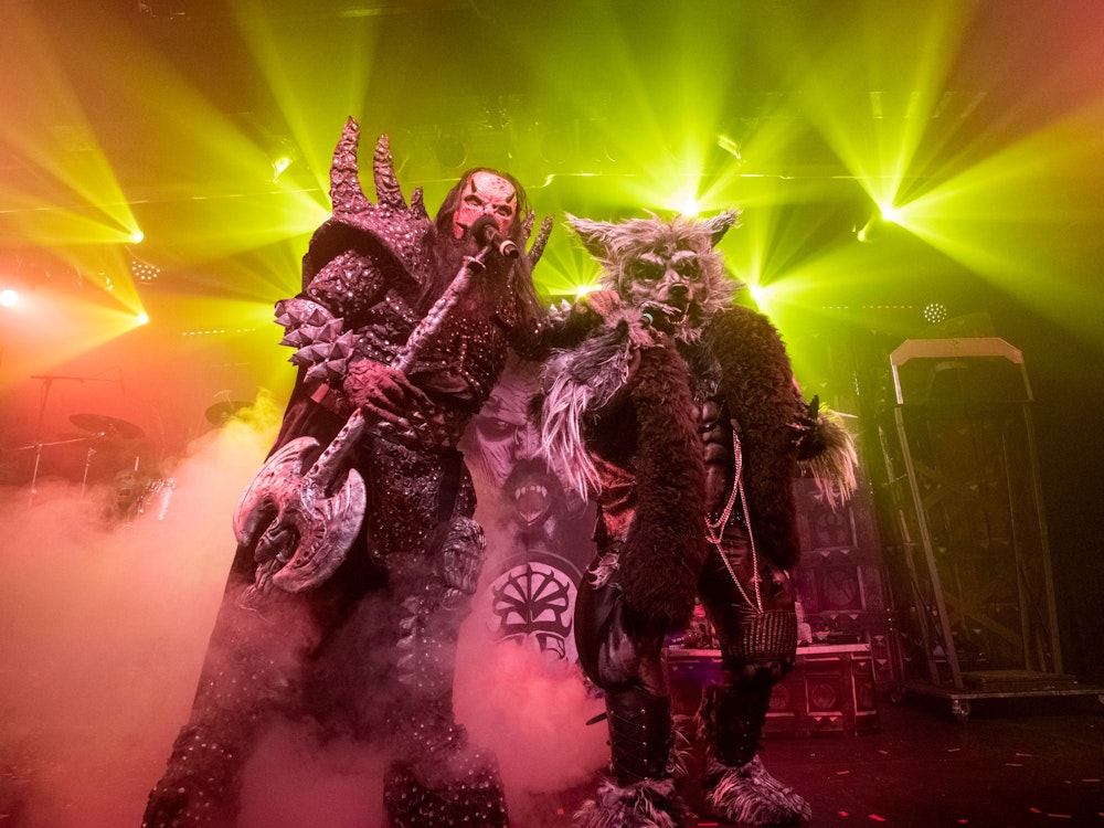 Der Sänger von Lordi und ein Mann im Werwolf-Kostüm stehen mit Mikrofonen auf der Bühne und singen.