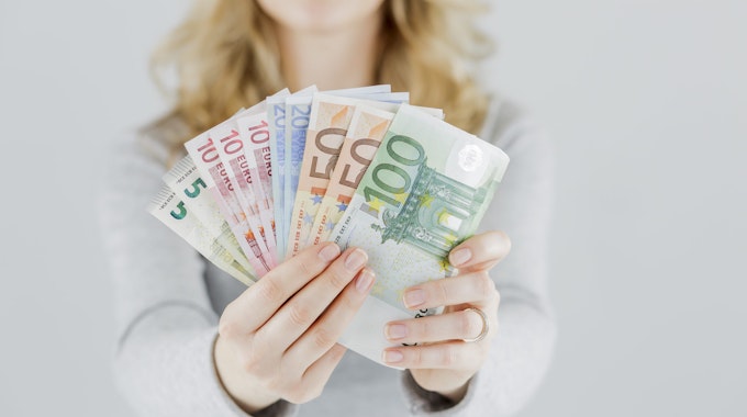 Eine Frau hält verschiedene Geldscheine in die Kamera, von fünf bis 100 Euro.