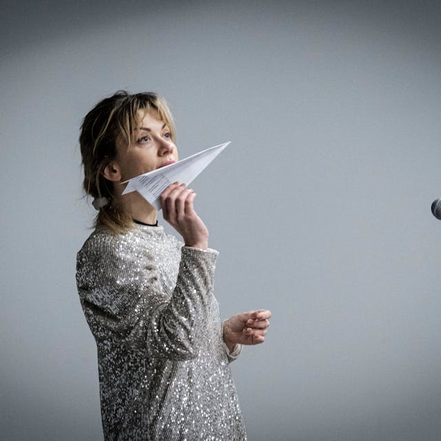 Die Schauspielerin Tetiana Zigura hält einen Papierflieger in der Hand und blickt nach oben.