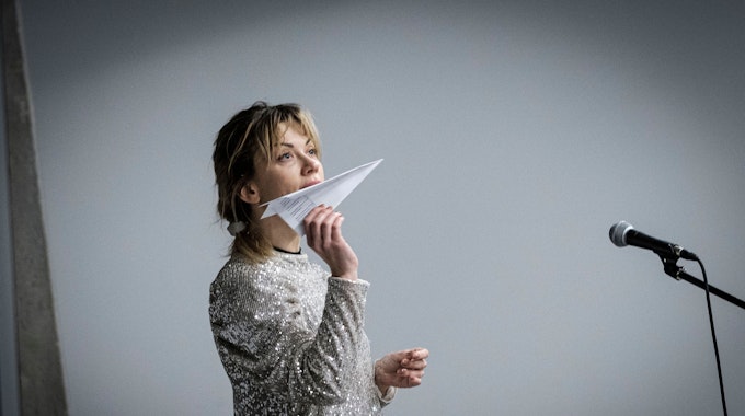 Die Schauspielerin Tetiana Zigura hält einen Papierflieger in der Hand und blickt nach oben.
