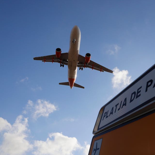 ARCHIV - 18.08.2020, Spanien, Palma: Ein Flugzeug überfliegt bei der Landung auf Mallorca ein Schild, das die Richtung nach Playa de Palma anzeigt.