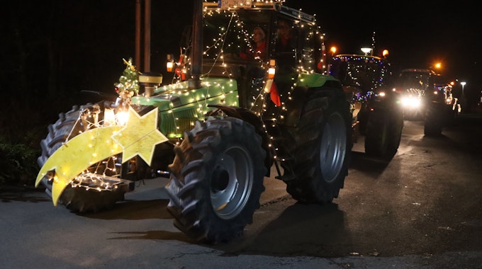 Weihnachtlich geschmückte Traktoren fahren in der Dunkelheit.