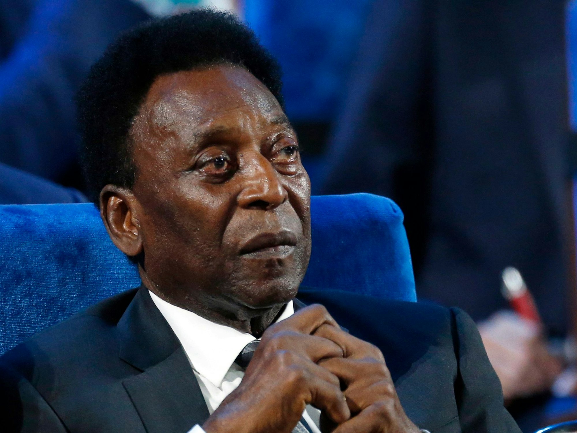 Pelé sitzt auf einer Veranstaltung im Anzug, hält die Hände zusammen.