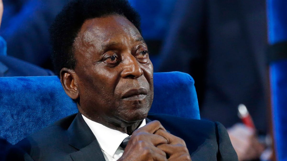 Pelé sitzt auf einer Veranstaltung im Anzug, hält die Hände zusammen.