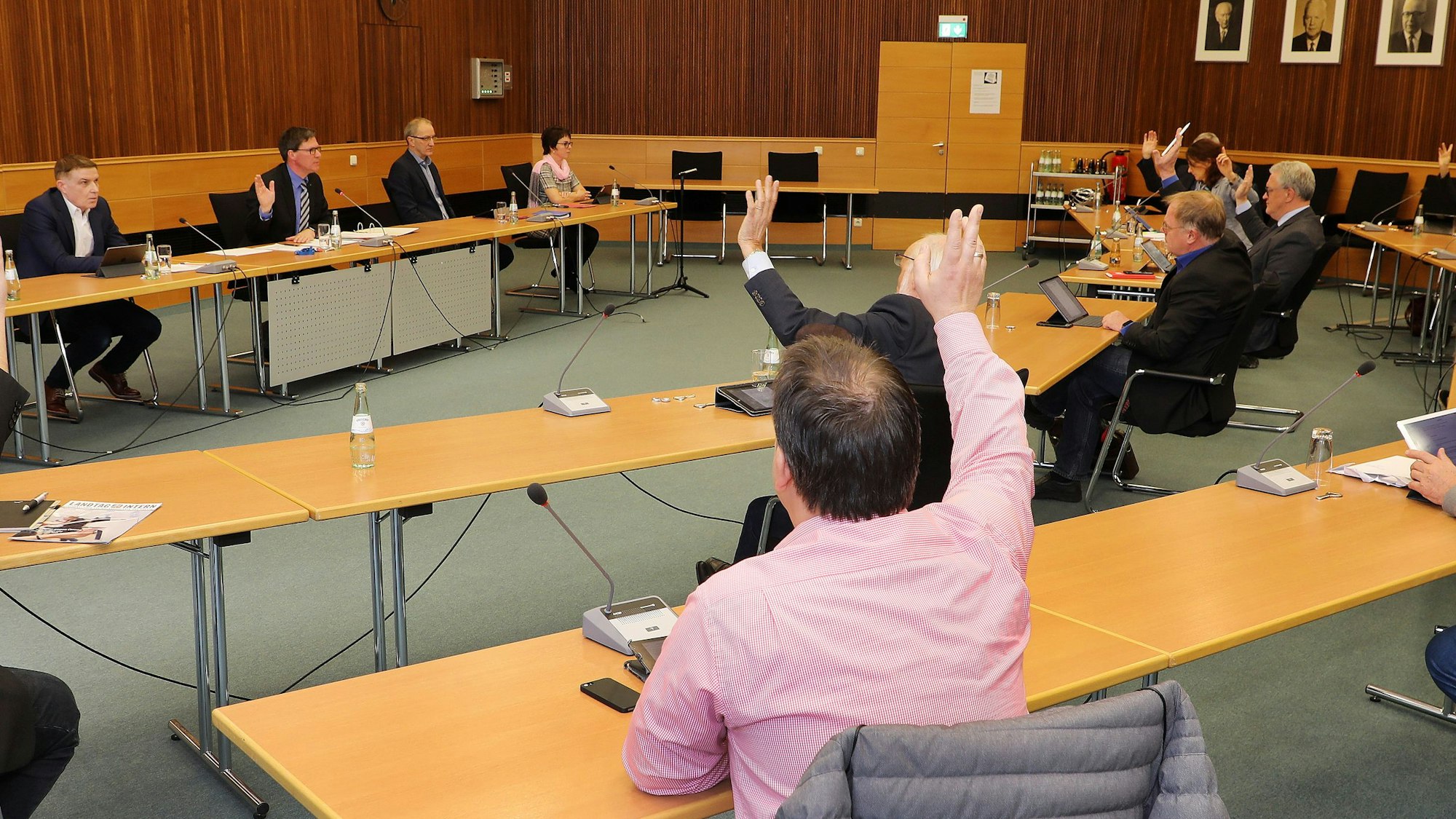 Der Kreisausschuss sitzt im Sitzungssaal in Bergisch Gladbach. Die Mitglieder heben die Hand zur Abstimmung, ebenso Landrat Stephan Santelmann.
