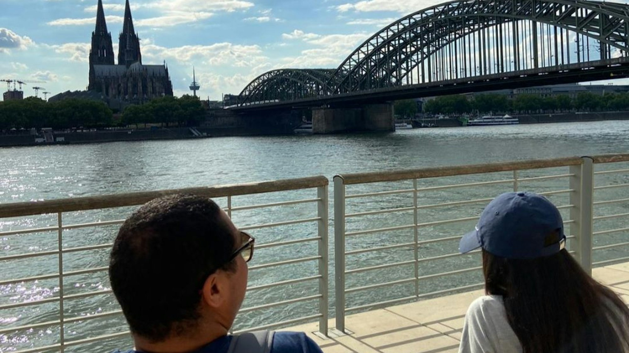 Zwei geflüchtete Jugendliche sitzen am Rhein und blicken auf den Kölner Dom.