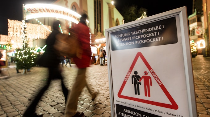 Symbolbild: 27.11.2017, Baden-Württemberg, Freiburg: Menschen gehen über den eröffneten Weihnachtsmarkt. Ein Schild warnt vor Taschendieben.