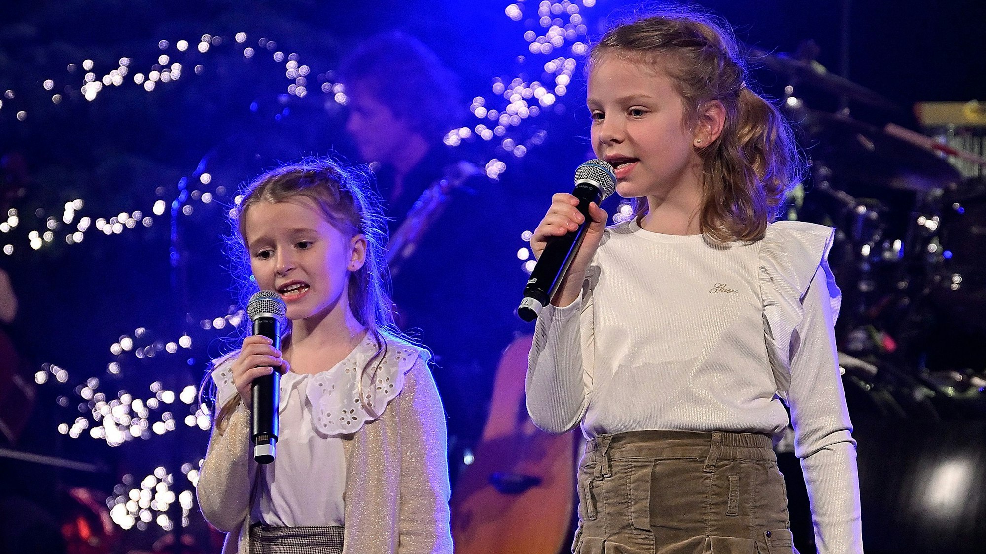Zwei Mädchen singen vor weihnachtlicher Kulisse.