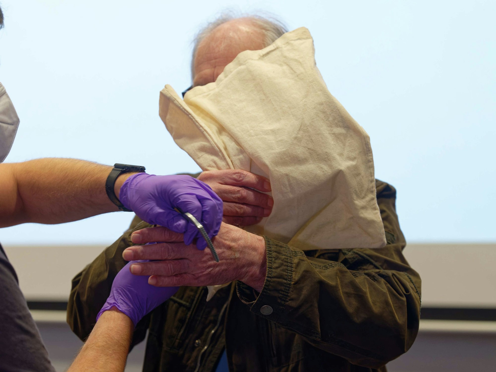 Dem Angeklagten werden zum Auftakt eines Prozesses wegen Mordes im Gerichtsaal im Landgericht in Bonn die Handschellen abgenommen. Er verdeckt sein Gesicht mit einer Tasche.