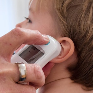Hand mit Fieberthermometer am Ohr eines Kleinkindes.