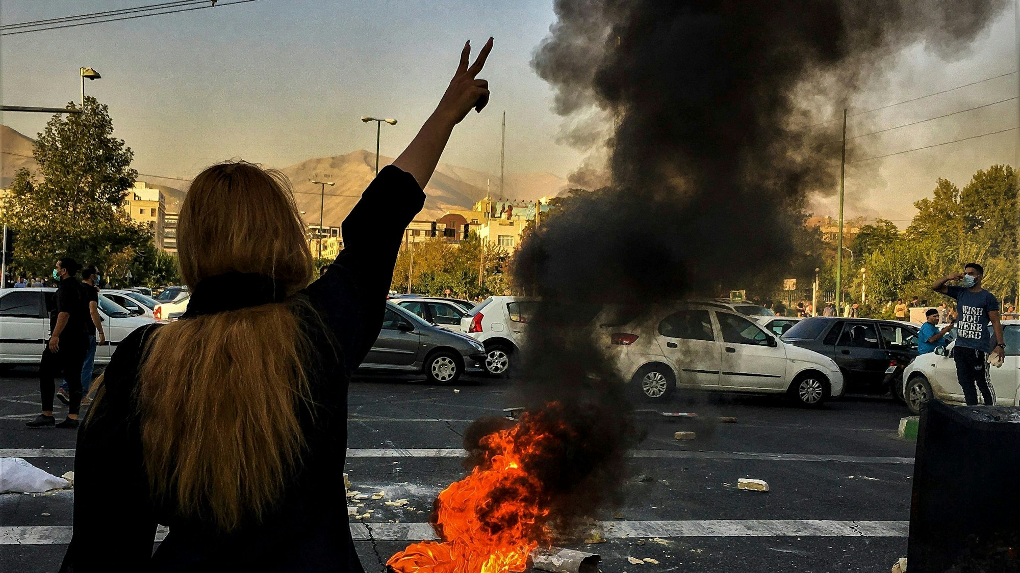 Eine Frau steht während einer Demonstration nach dem Tod der 22-jährigen Mahsa Amini vor einem brennenden Autoreifen und zeigt das Victory-Zeichen.
