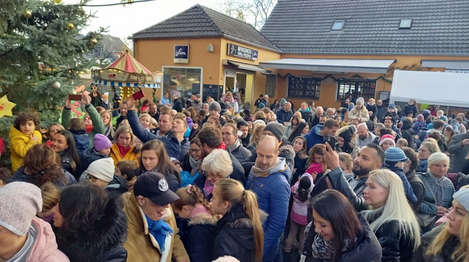Eine große Menschenmenge ist zu sehen, im Hintergrund ein gelbes Gebäude, links Teile eines großen Weihnachtsbaumes.