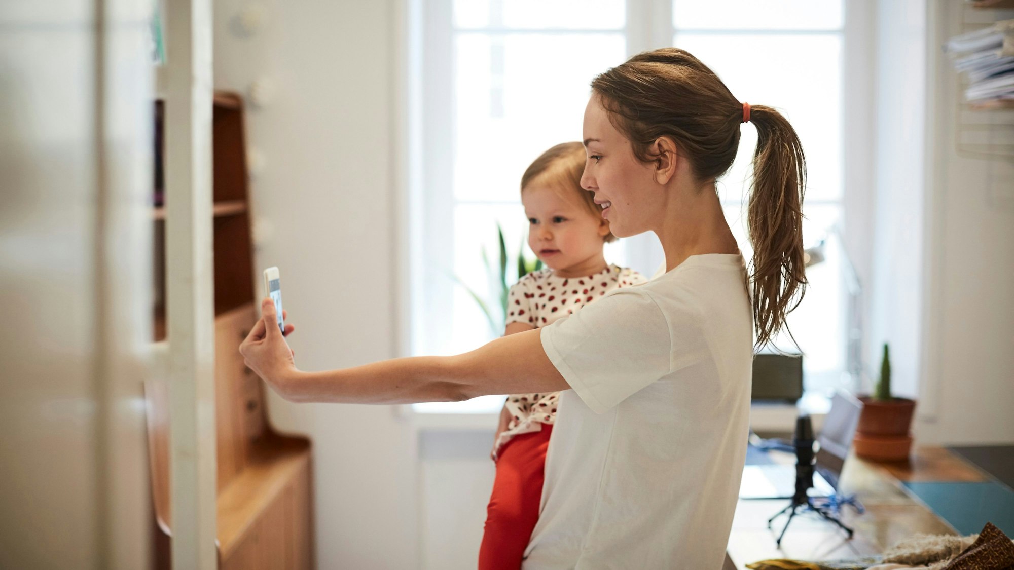 Influencerin nimmt ein Selfie mit ihrer Tochter auf Symbolbild.