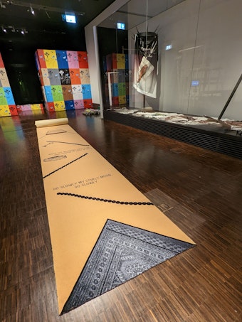Ein langer Teppich mit Liedzeilen und Symbolen, mit dem die Künstlerin Donja Nasseri den familiären Druck auf heiratsfähige Frauen thematisiert.