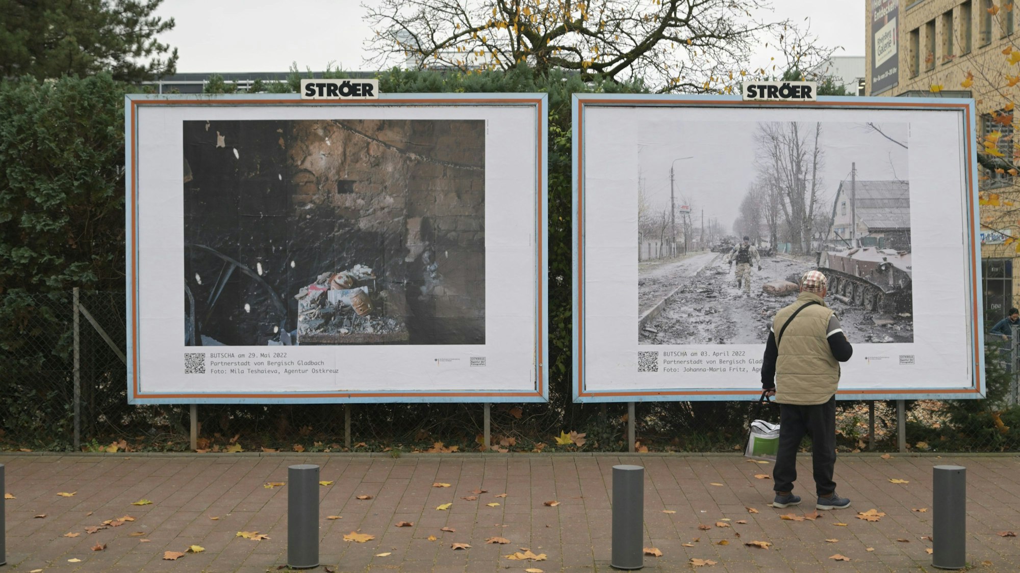 Ein Mann steht vor den beiden großformatigen Bildern, die in Bergisch Gladbach gegenüber dem Busbahnhof hängen.