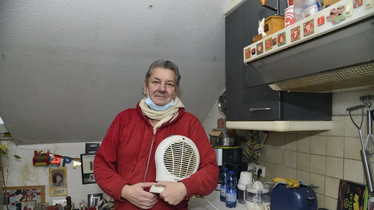 Harald Berndt steht mit Schal in seiner Küche und hält einen Heizlüfter in den Händen.