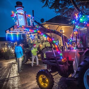 Zwei mit bunten Lichterketten und einem beleuchteten Schneemann dekorierte Traktoren fahren auf der Atzlenbacher Straße an Zuschauern vorbei.