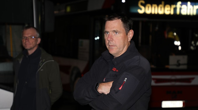 Feuerwehrchef Jörg Köhler steht im Dunkeln mit verschränkten Armen vor einem Bus, dessen Anzeige „Sonderfahrt“ anzeigt. Im Hintergrund steht Bürgermeister Frank Stein.