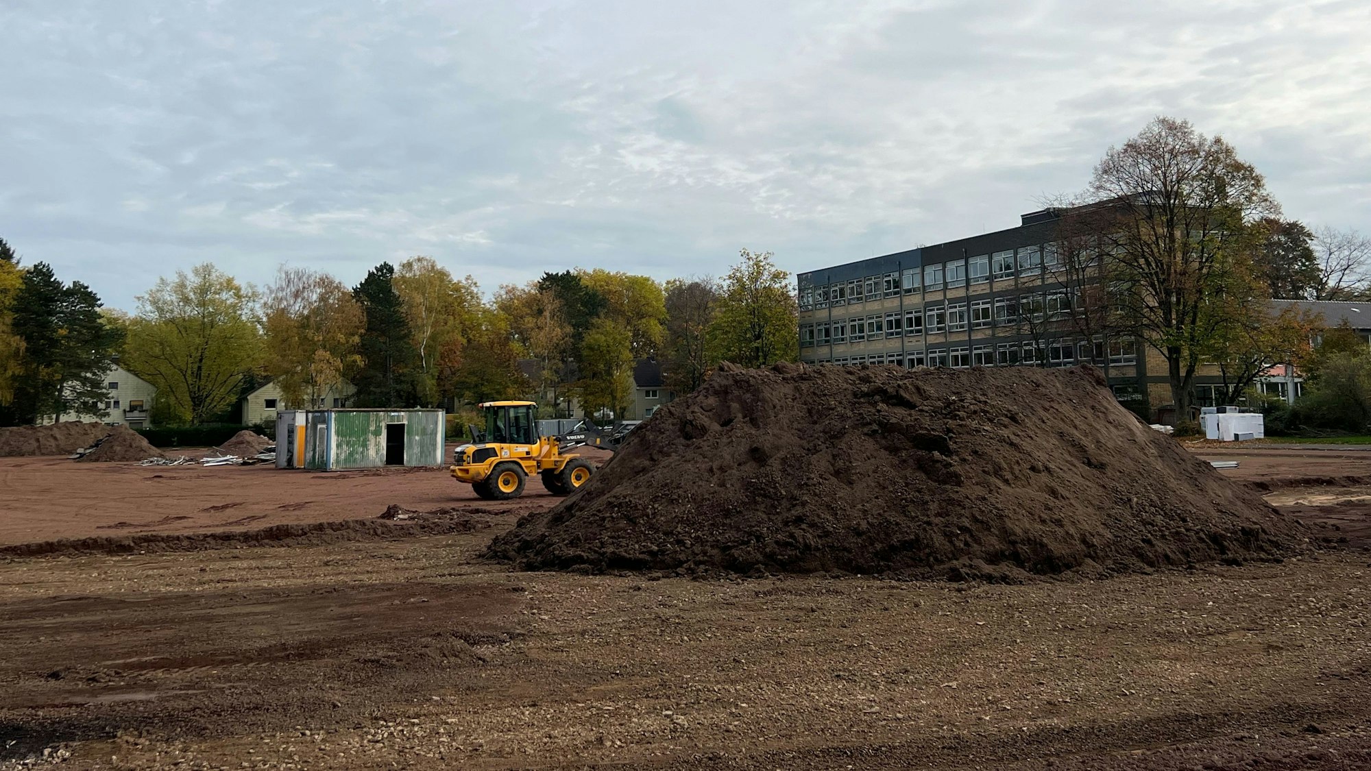 Die Arbeiten für den neuen Sportplatz am Stadtgymnasium laufen. Neben einem Hügel Erde steht ein Bagger auf der Baustelle.