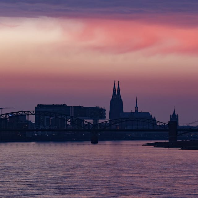 Das Bild zeigt den Blick auf Köln in der Dämmerung, zu sehen sind der Dom, die Brücken und die Kranhäuser.