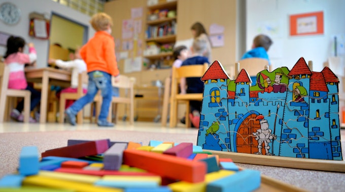 Spielzeug liegt in einer Kindertagesstätte auf dem Boden. Im Hintergrund sind Kinder zu erkennen.