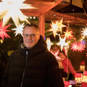 Mathias Klabunde steht unter leuchtenden Sternen auf einem Kölner Weihnachtsmarkt.