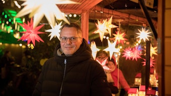 Mathias Klabunde steht unter leuchtenden Sternen auf einem Kölner Weihnachtsmarkt.