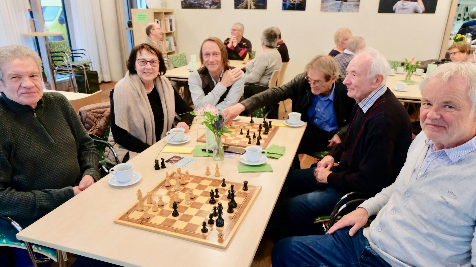 Mitglieder der Sülzer Schachmeile sitzen in einem Café an einem Tisch mit zwei Schachbrettern.