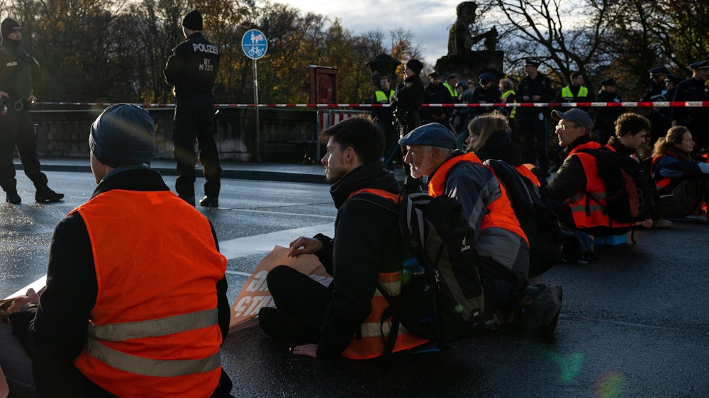 In einer Reihe sitzen Klimaaktivisten der Umweltschutzbewegung „Letzte Generation“ sitzen auf der Münchner Prinzregentenstraße und blockieren den Verkehr.