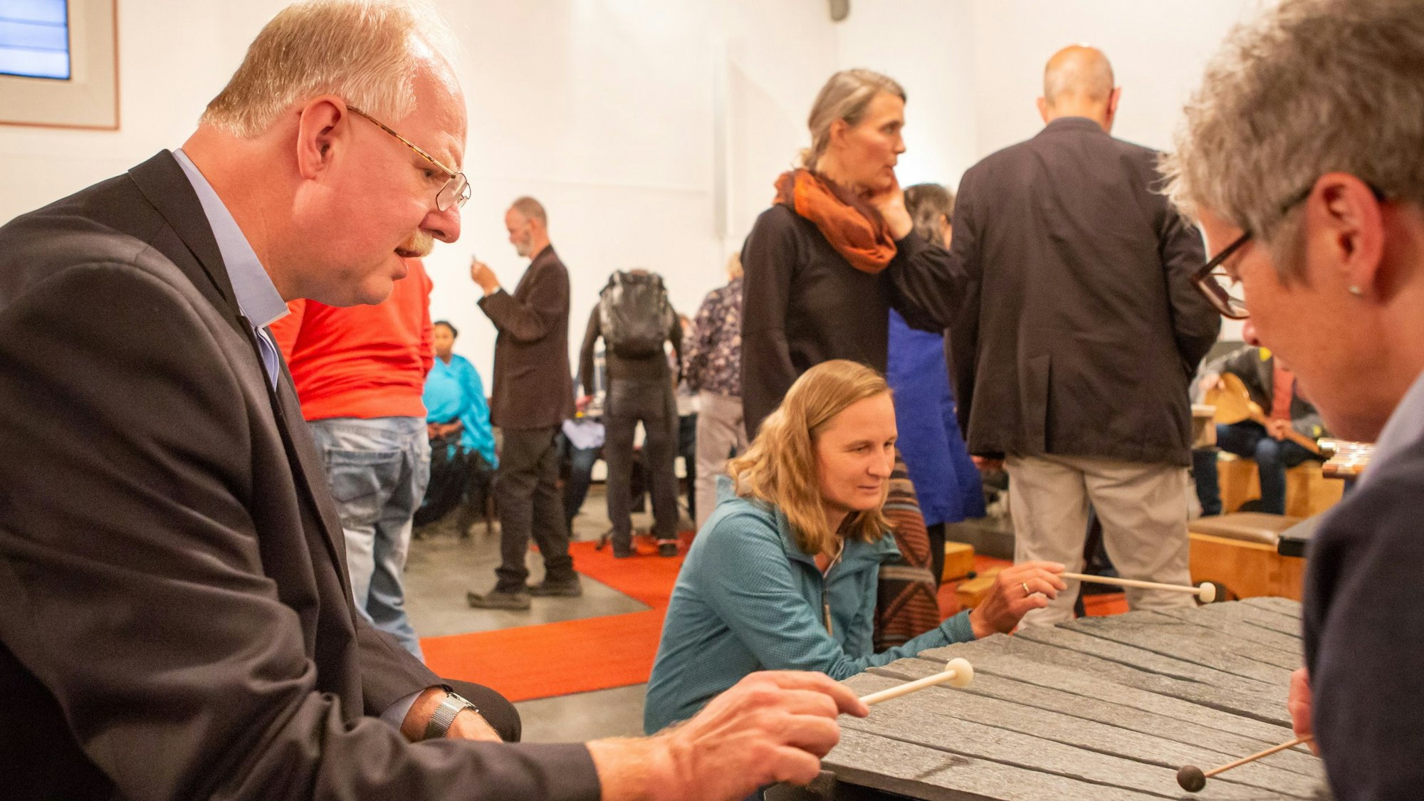 Christoph Bersch spielt mit zwei Frauen ein Musikinstrument. Im Hintergrund sind mehrere kleine Personen zu sehen.