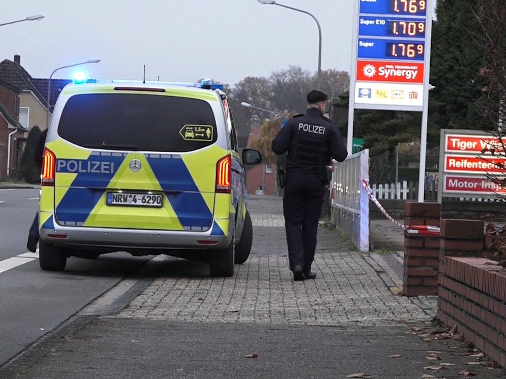 Ein Polizeifahrzeug steht vor einer Tankstelle in Lengerich, daneben steht ein Polizist.