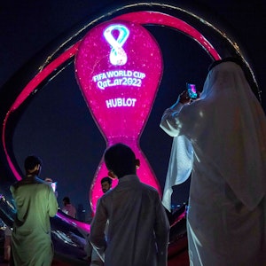 Feierlichkeiten bei einer Werbe-Veranstaltung im Vorfeld der WM 2022 in Katar. Ein leuchtend angestrahlter überdimensionaler WM-Pokal wird von mehreren Personen fotografiert.