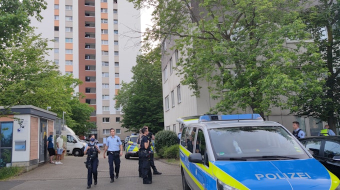 Polizeikräfte stehen vor einem Gebäude in der Gernsheimer Straße in Köln-Ostheim. Neben ihnen steht ein Polizeiwagen.