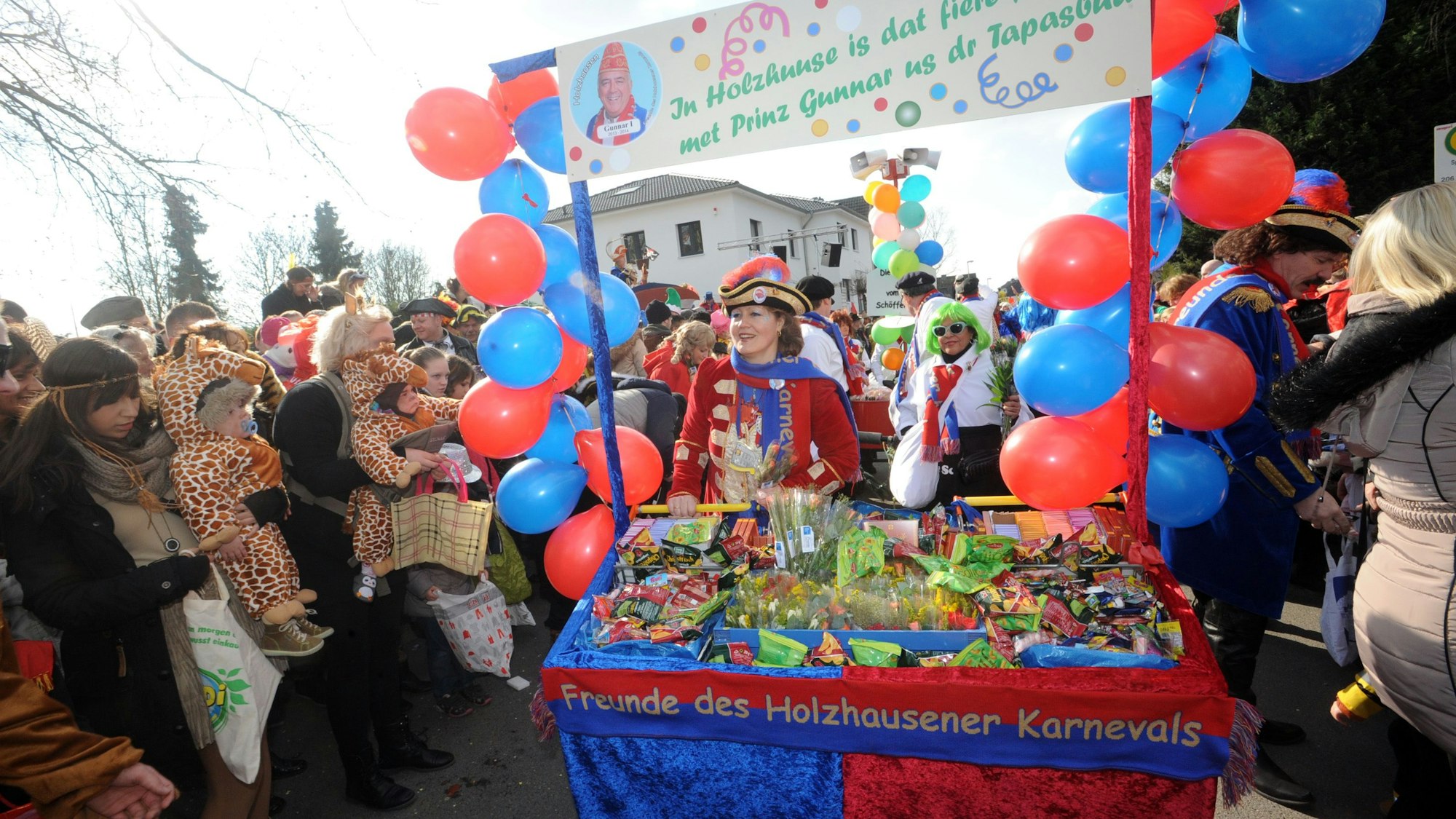 Der Karnevalszug in Holzhausen. Links und rechts bunt kostümierte Menschen, in der Mitte ein rot-blauer Karnevalswagen der „Freunde des Holzhausener Karnevals“.