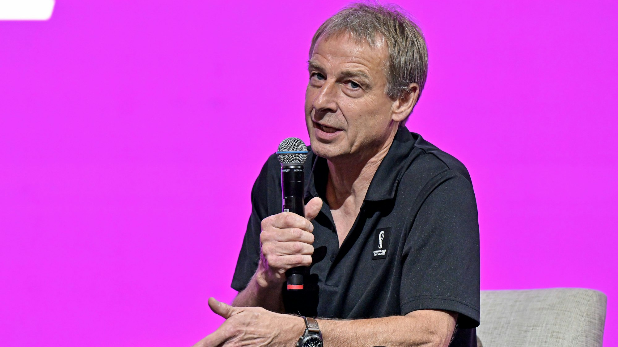 Jürgen Klinsmann hält auf einer Pressekonferenz der FIFA in Doha ein Mikrofon in der Hand und spricht