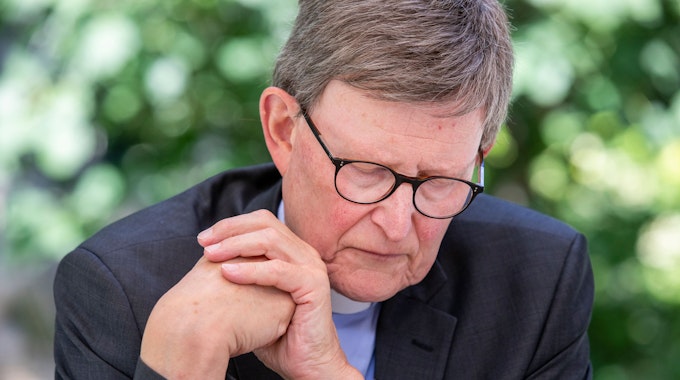 Der Kölner Erzbischof, Kardinal Rainer Woelki, sitzt mit gesenktem Blick und ineinander geschlagenen Händen im Garten des erzbischöflichen Hauses.