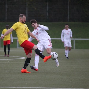 Ein Euskirchener Spieler in einem gelb-roten Trikot schießt den Ball aus der Gefahrenzone.