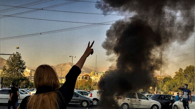Eine Demonstrantin Teheran steht ohne Kopftuch vor einer brennenden Mülltone.