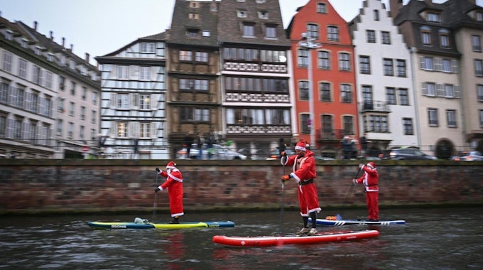 Verkleidet als Weihnachtsmänner paddeln mehrere Männer mit SUP-Boards durch den Fluss Ill in Straßburg.