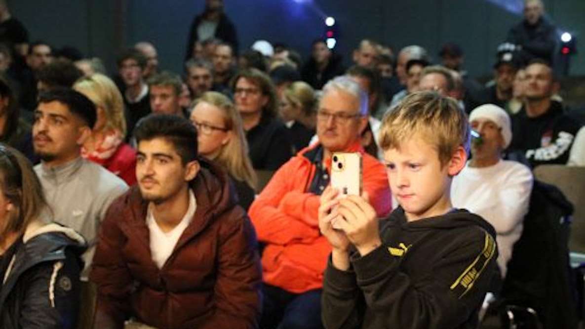 Viele Zuschauer füllen die Ränge bei der Mechernicher Fight Night. In der ersten Reihe filmt ein Junge mit dem Handy mit.