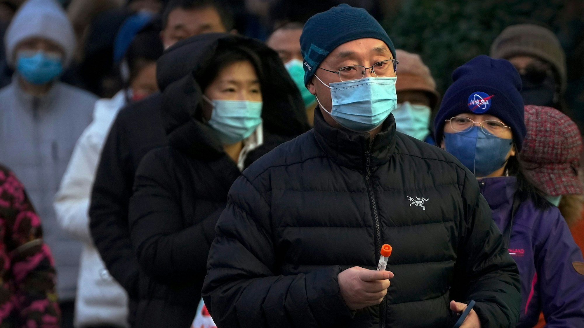 Ein Mann mit Gesichtsmaske hält ein Corona-Teströhrchen. Er steht mit anderen Bewohnern Pekings in einer Warteschlange, um einen Coronatest zu machen