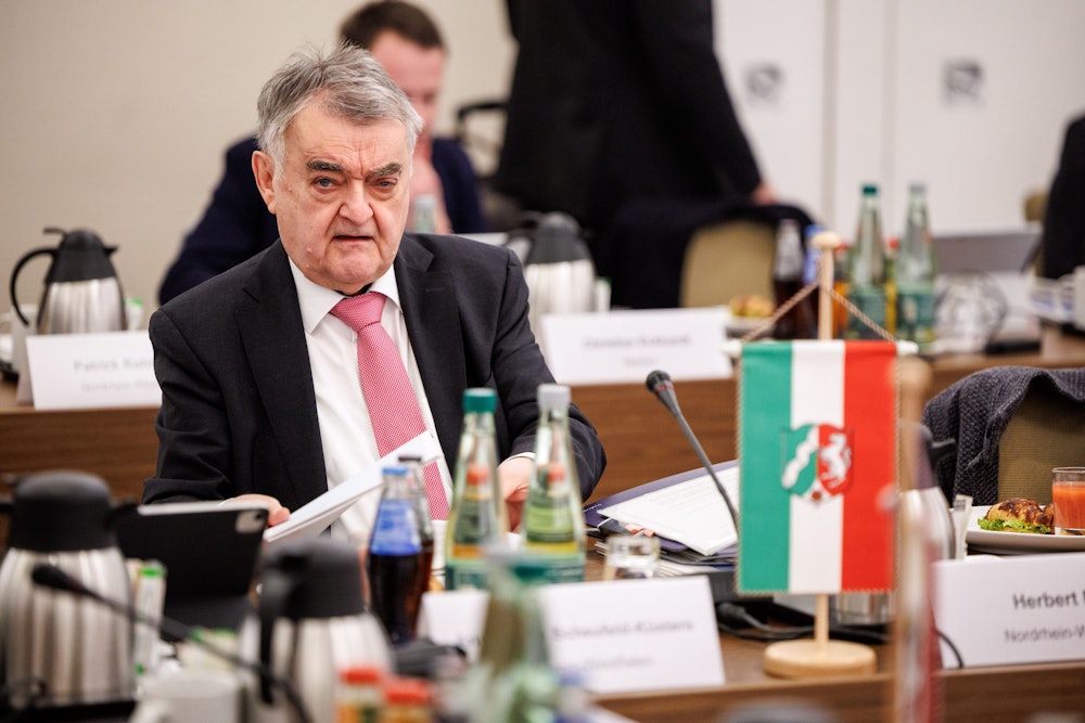 NRW-Innenminister Herbert Reul sitzt im Anzug bei einer Konferenz.