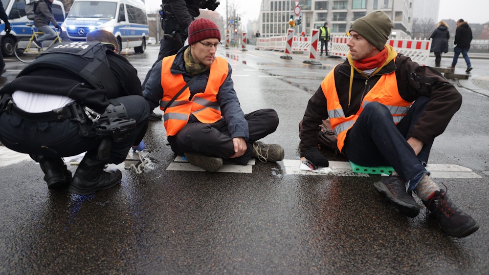 Polizisten lösen die Hand eines Klimaaktivisten vom Asphalt auf der Invalidenstraße in Berlin. Aktivisten der "Letzten Generation" hatten sich im Berufsverkehr mit einer Hand auf die Fahrbahn geklebt, um gegen die Klimapolitik der Bundesregierung zu protestieren.