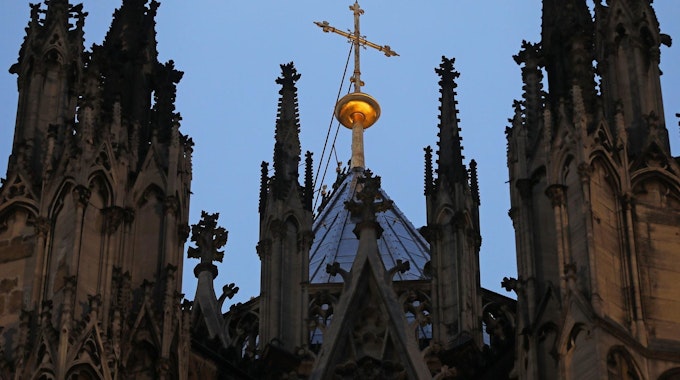 Köln: Ein Kreuz steht hinter dem Strebewerk am Kölner Dom (Archivbild).