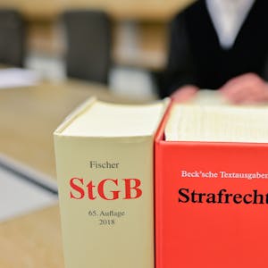 Ein Richter sitzt in einem Sitzungssaal des Gerichts hinter Büchern mit der Aufschrift „StGB“ und „Strafrecht“.