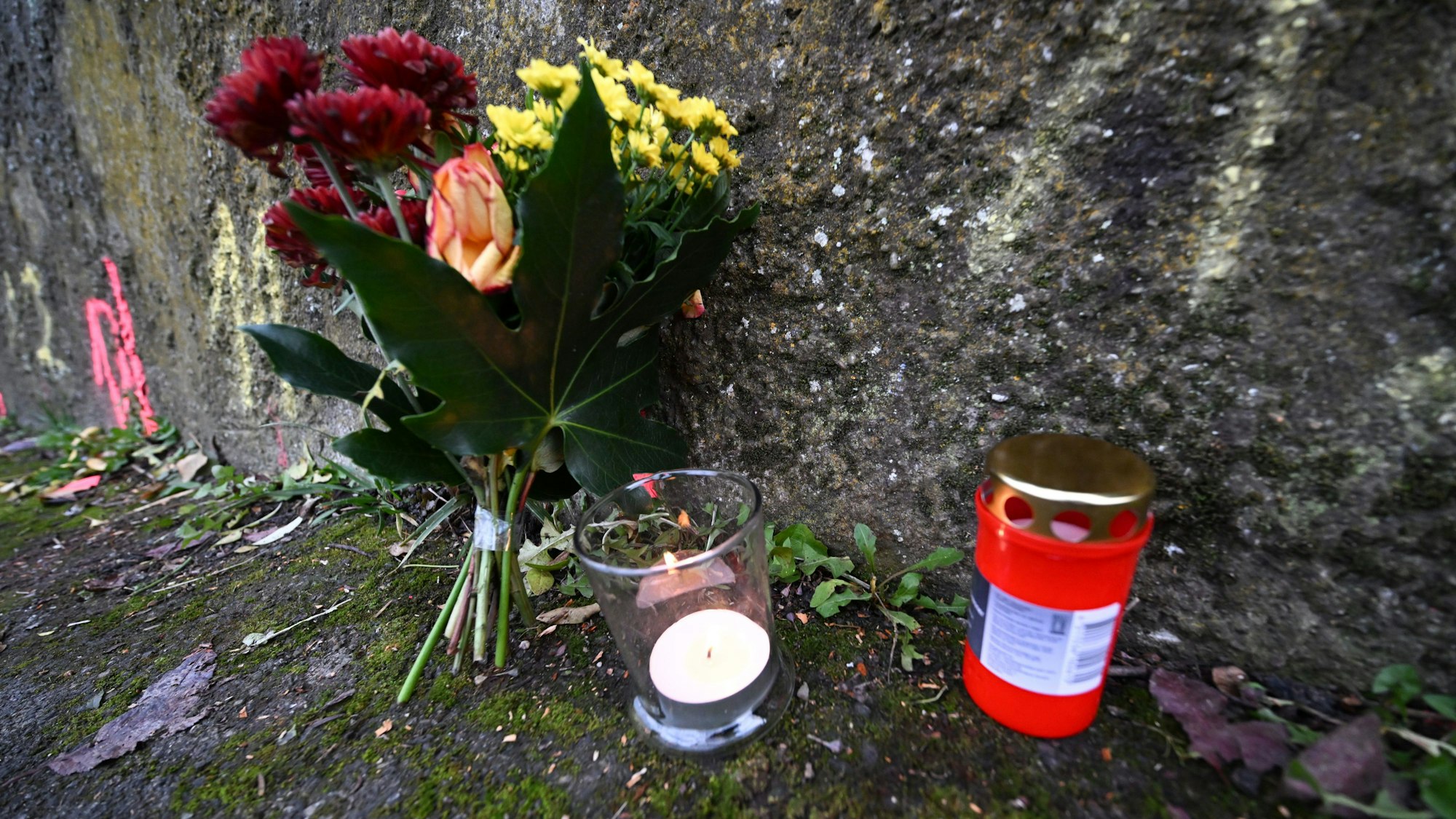 Baden-Württemberg, Illerkirchberg: Blumen und Kerzen stehen an Markierungen der Spurensicherung der Polizei an einem Tatort auf einem Weg.