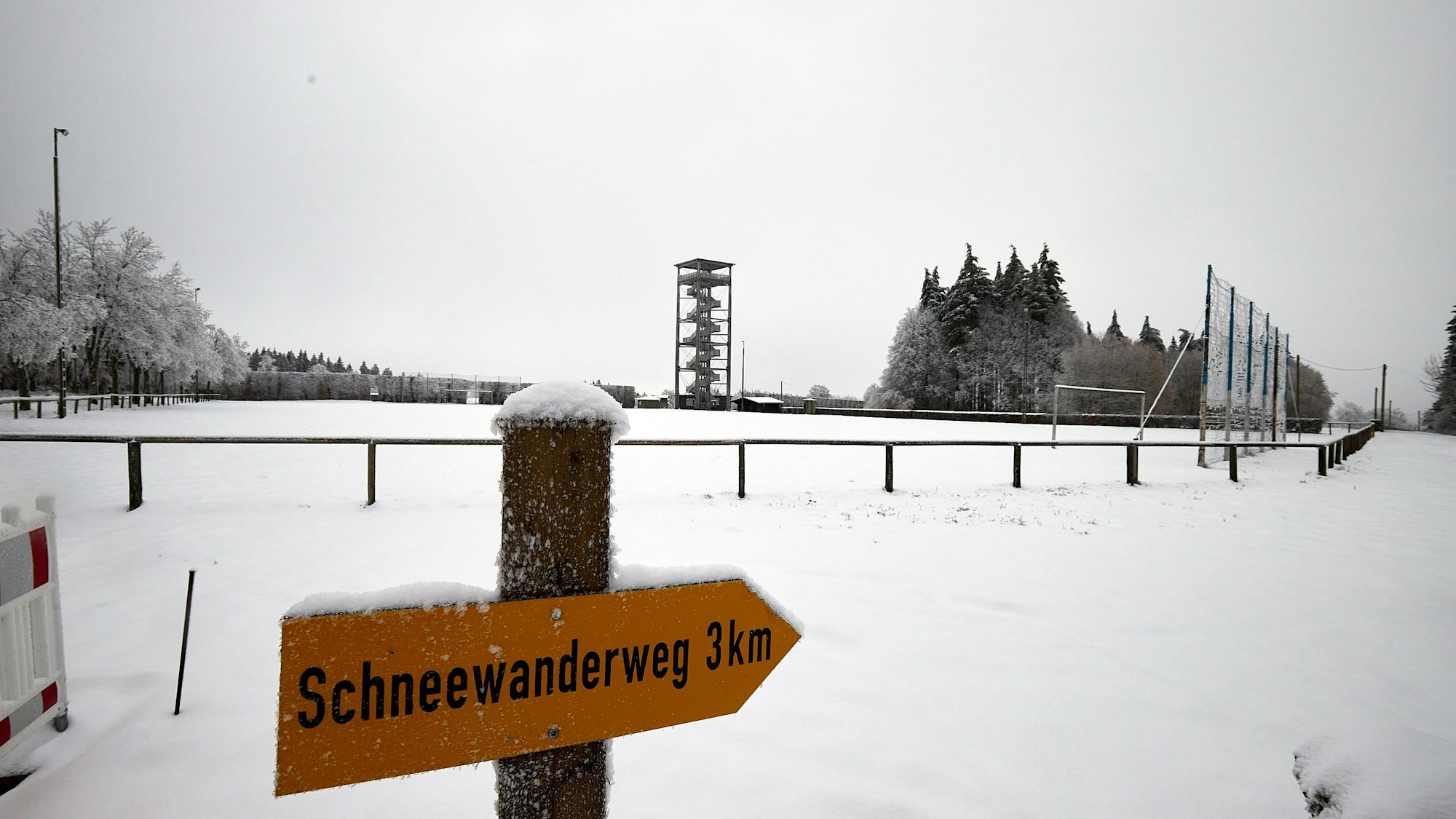 Ein Schild weist Wanderern den Weg zu einer drei Kilometer langen Schneewanderung. Im Hintergrund ist der Aussichtsturm am Weißen Stein bei Udenbreth zu sehen.