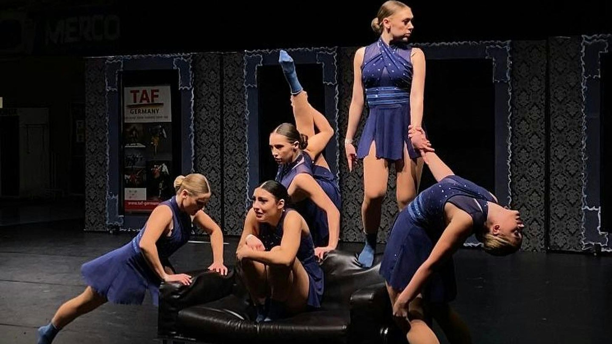 Fünf Tänzerinnen in blauen Kleidern auf der Bühne.