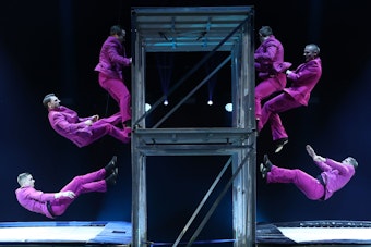 Am Double Trampoline Wall springt die Truppe Yakubovskii zu knallhartem Techno-Sound - sechs Männer in lila Anzügen stehen in der Luft.